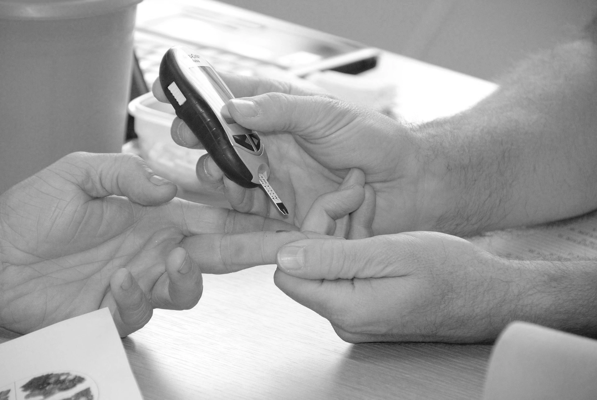A clinician holding a glucose meter beside a patient's fingertip