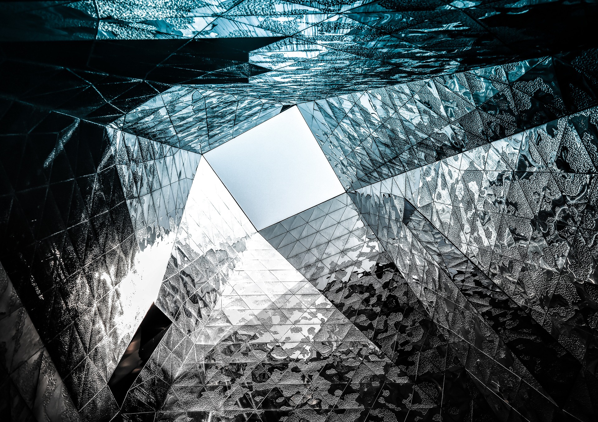 Looking up through a faceted atrium of mirrored panels toward the sky