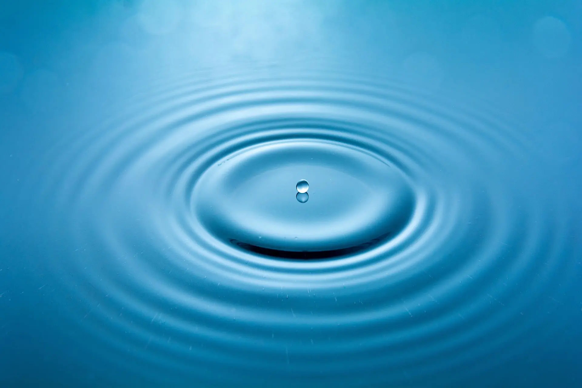 A single water drop falling into still water, sending out rings of ripples