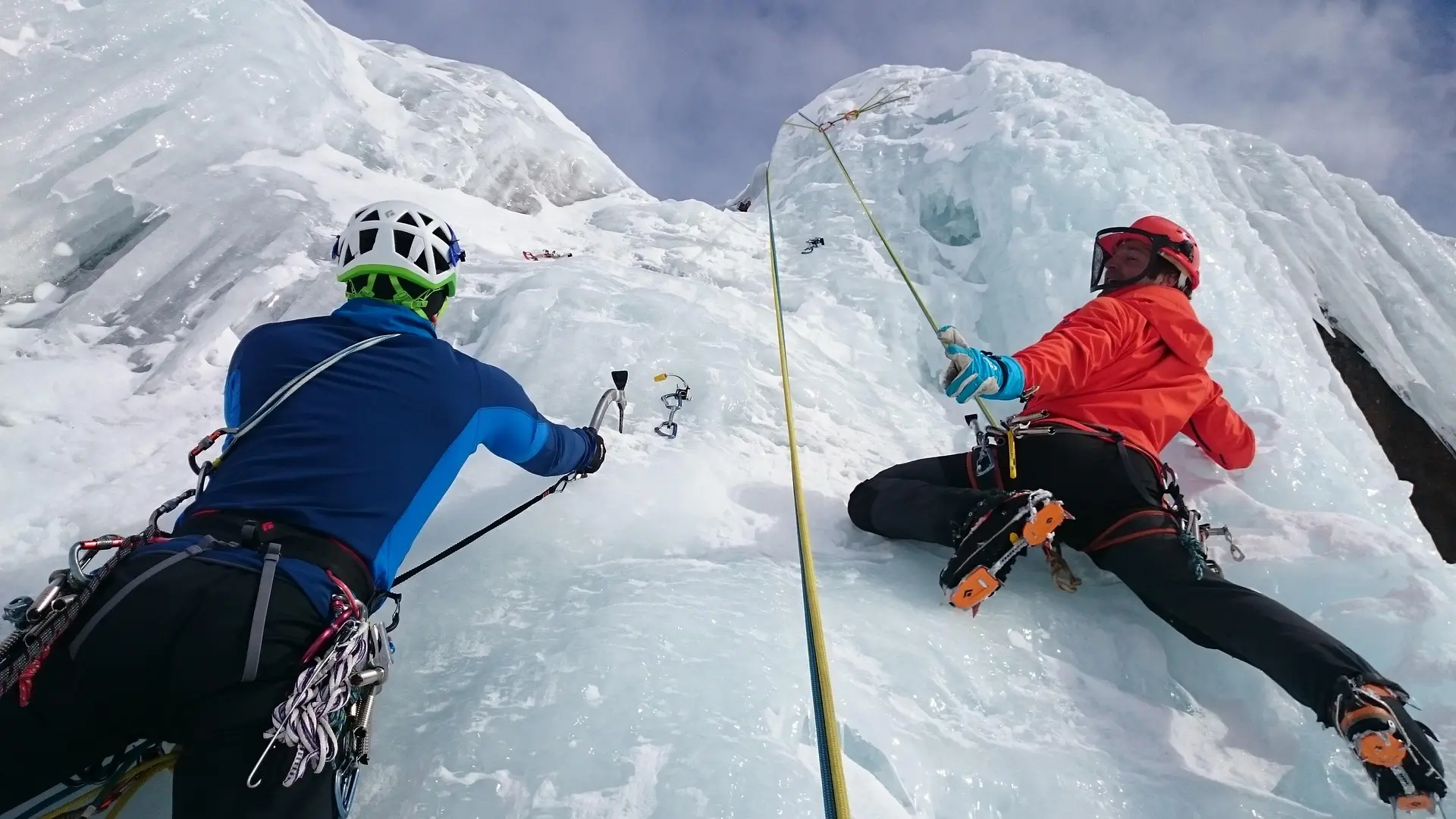 Two ice climbers roped together, one belaying the other up a frozen wall